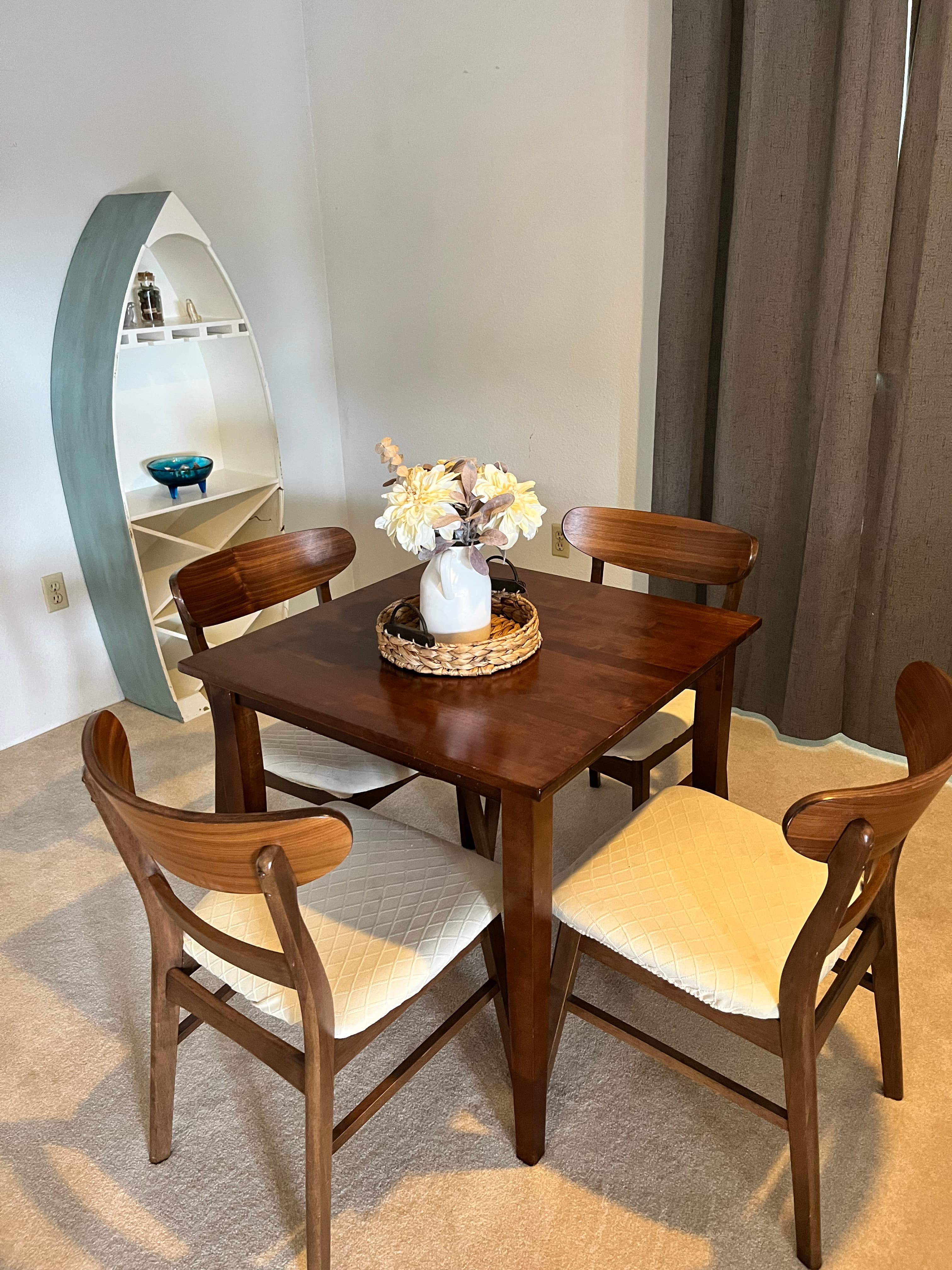 Square dark wood dining table with four chairs and a unique boat-shaped bookshelf in the corner.
