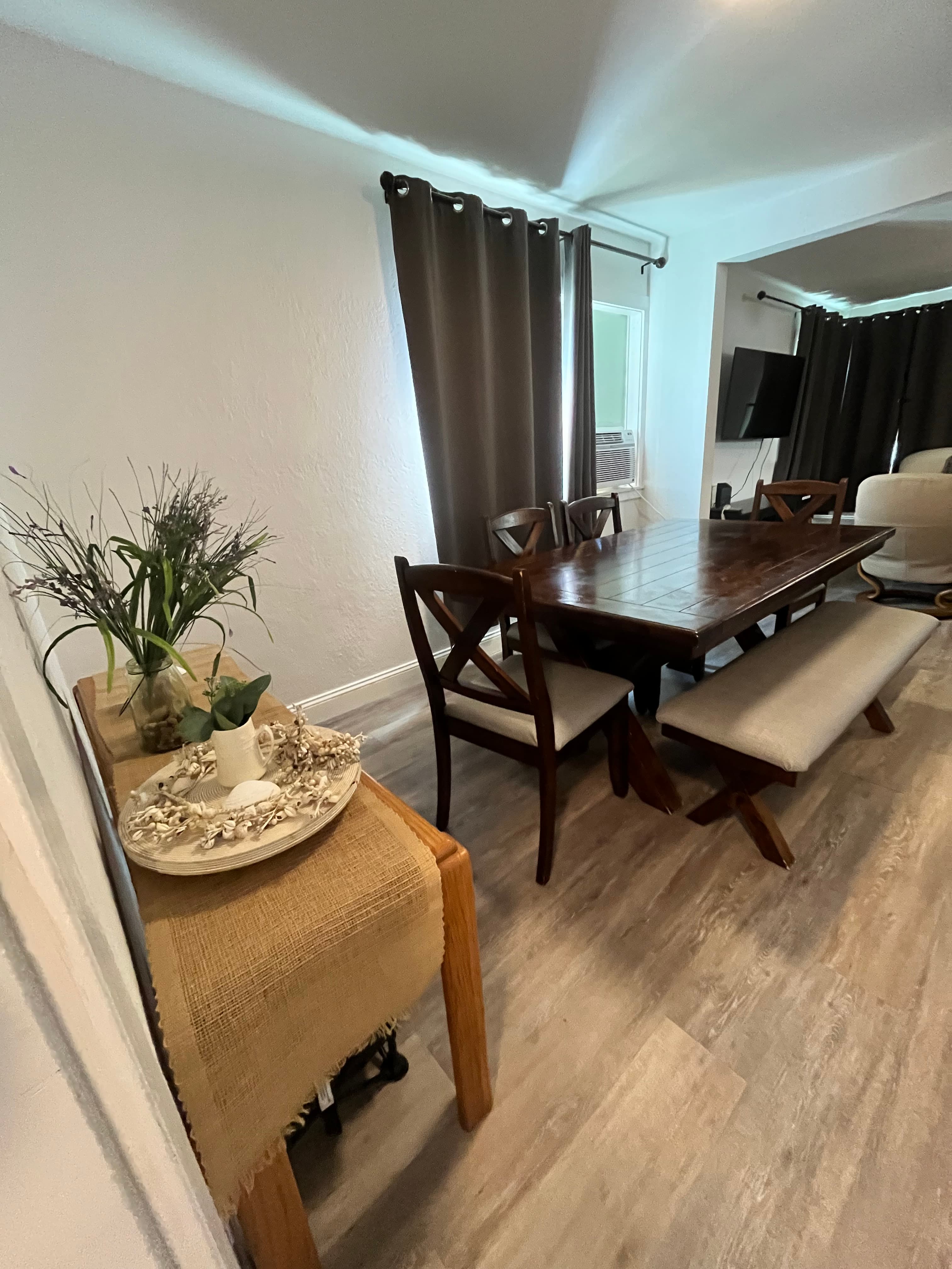 Dark wood dining table with X-back chairs and bench beside a decorated wooden side table.
